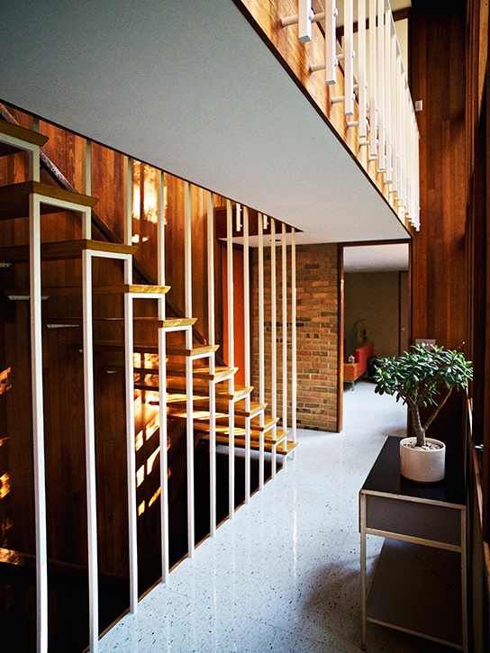 A staircase with treads cantilevered from the redwood wall and suspended by a bank of ceiling-height balusters. 